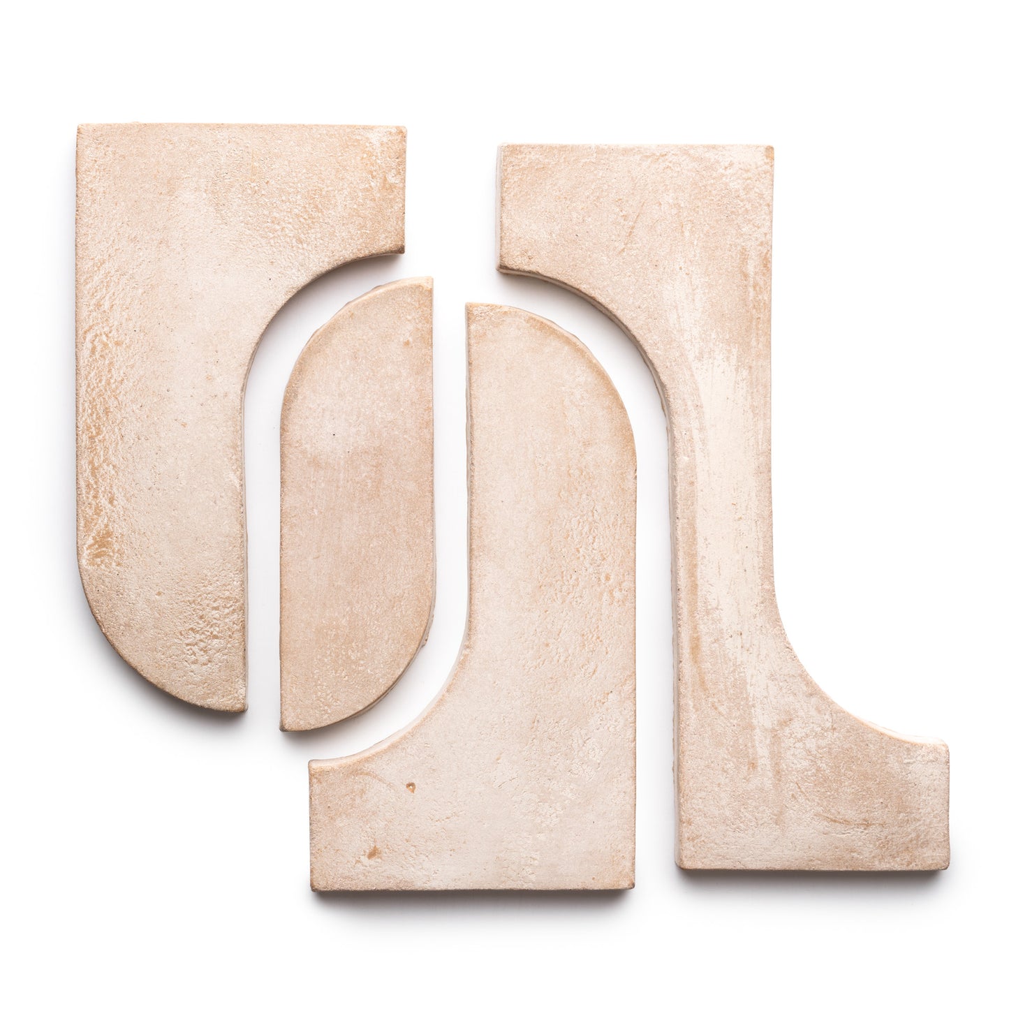 Four Durango + Blanco beige ceramic tiles from Zia Tile, featuring curved and straight edges, are arranged on a white background to create an abstract geometric pattern.