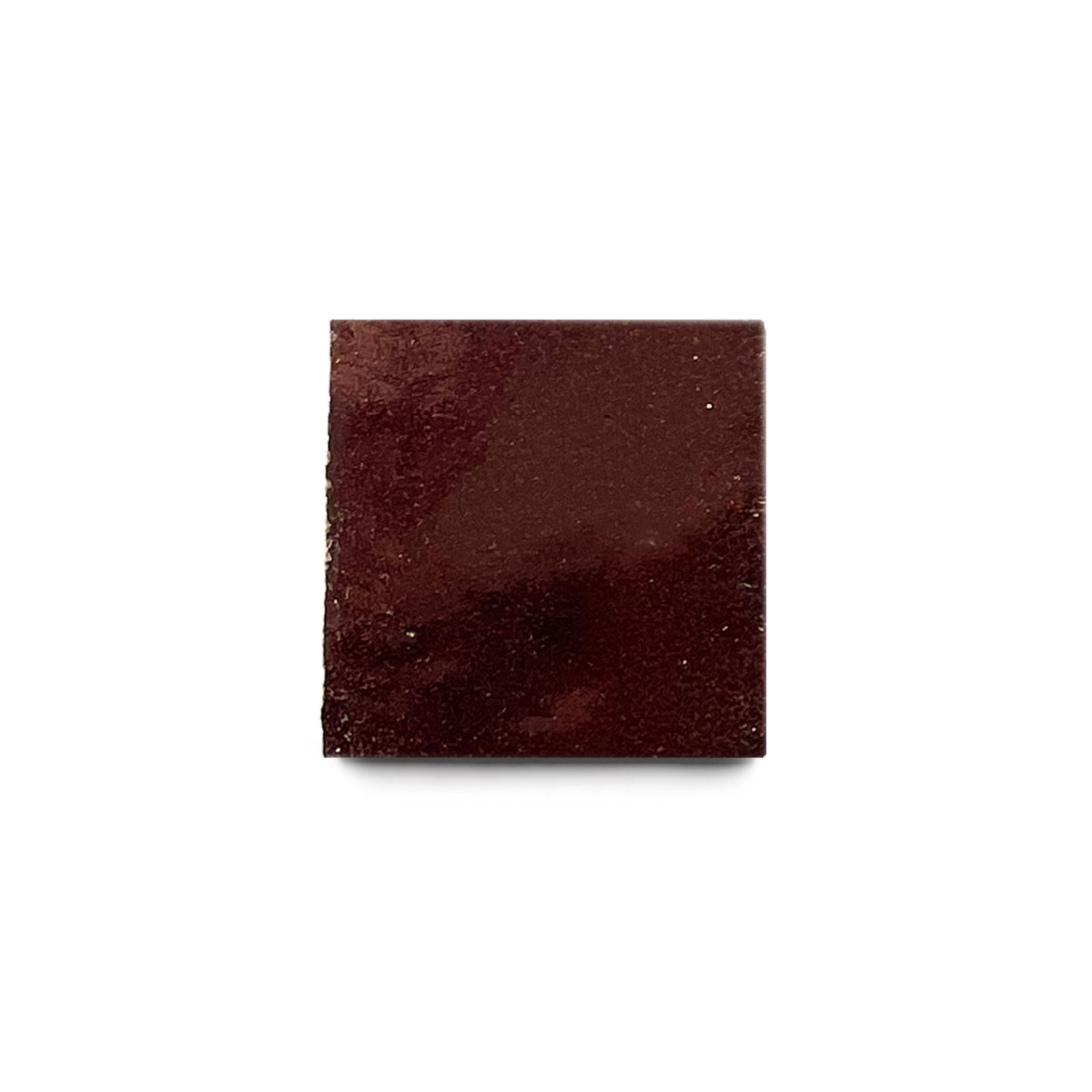 A single square piece of dark chocolate is centered on a white background, echoing the deep, warm tones of Burnt Sugar 2x2 tile.