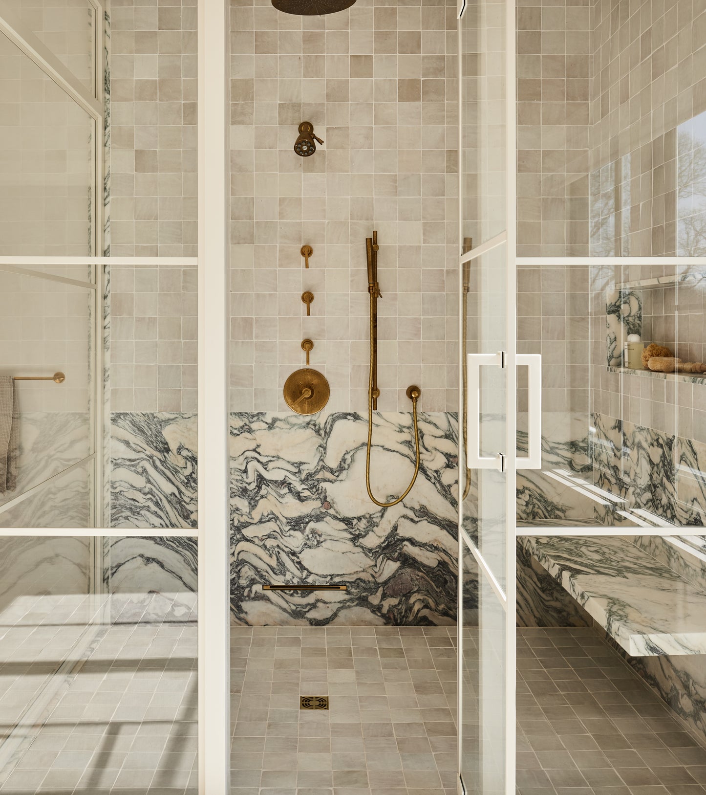 Modern shower with glass doors, brass fixtures, and a marble bench. Soft natural light highlights walls adorned with Casablanca 4x4 tiles from vendor-unknown, adding texture and character for a luxurious, minimalist look.