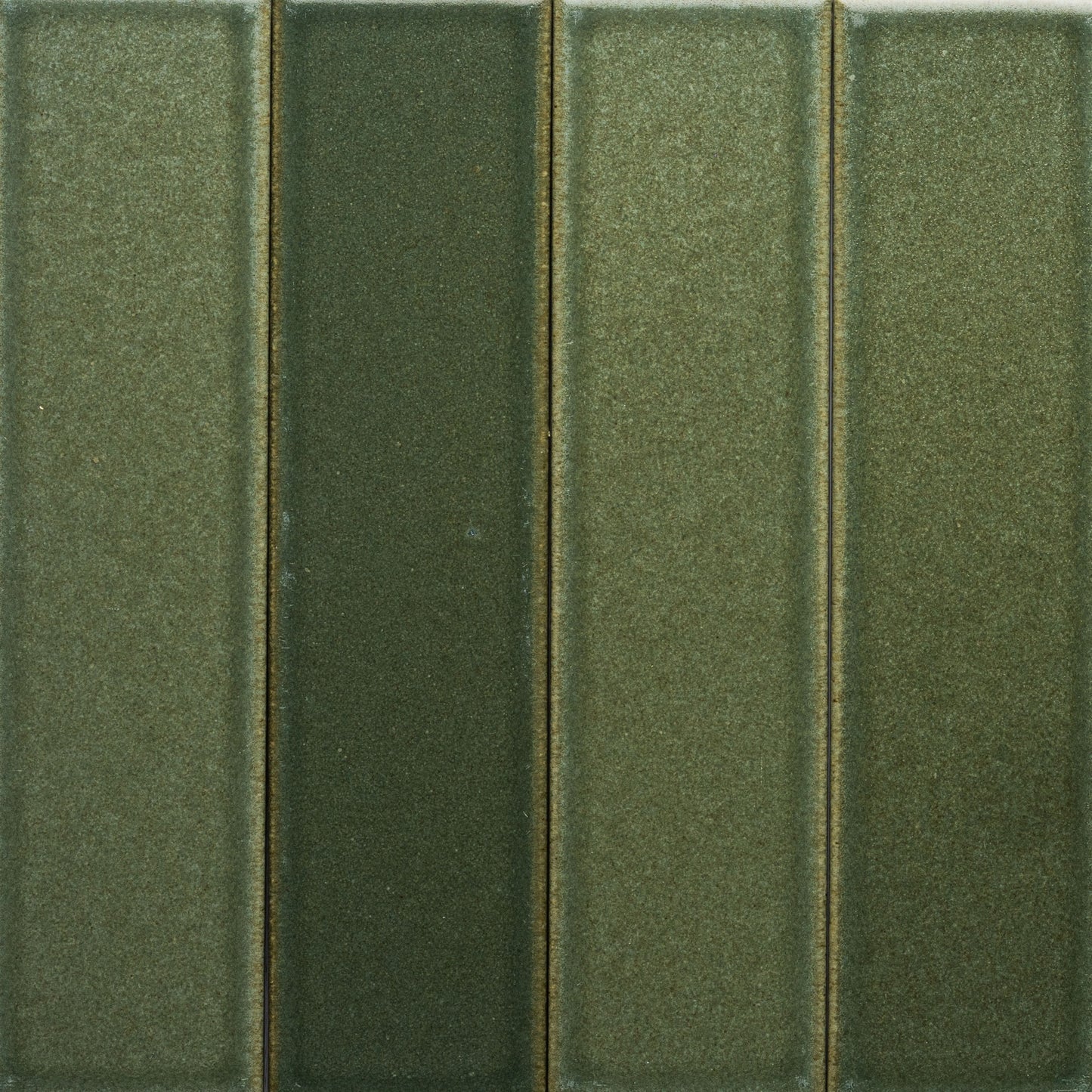 A close-up of four vertical, rectangular Frogtown + Flat green tiles by Zia Tile, each in slightly different shades, arranged side by side with a smooth, matte finish and subtle texture.