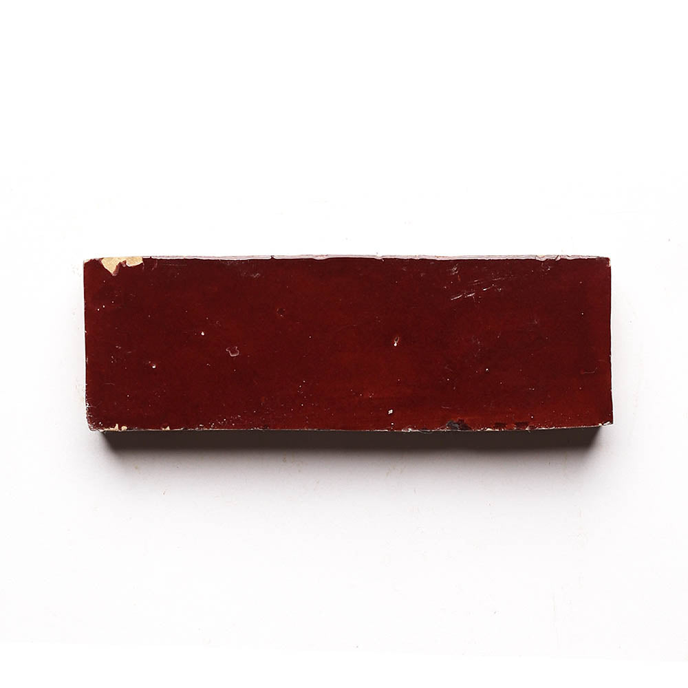 A single rectangular Rouge 2x6 red brick tile with slightly chipped edges, displayed against a plain white background—ideal for adding character to a kitchen backsplash.