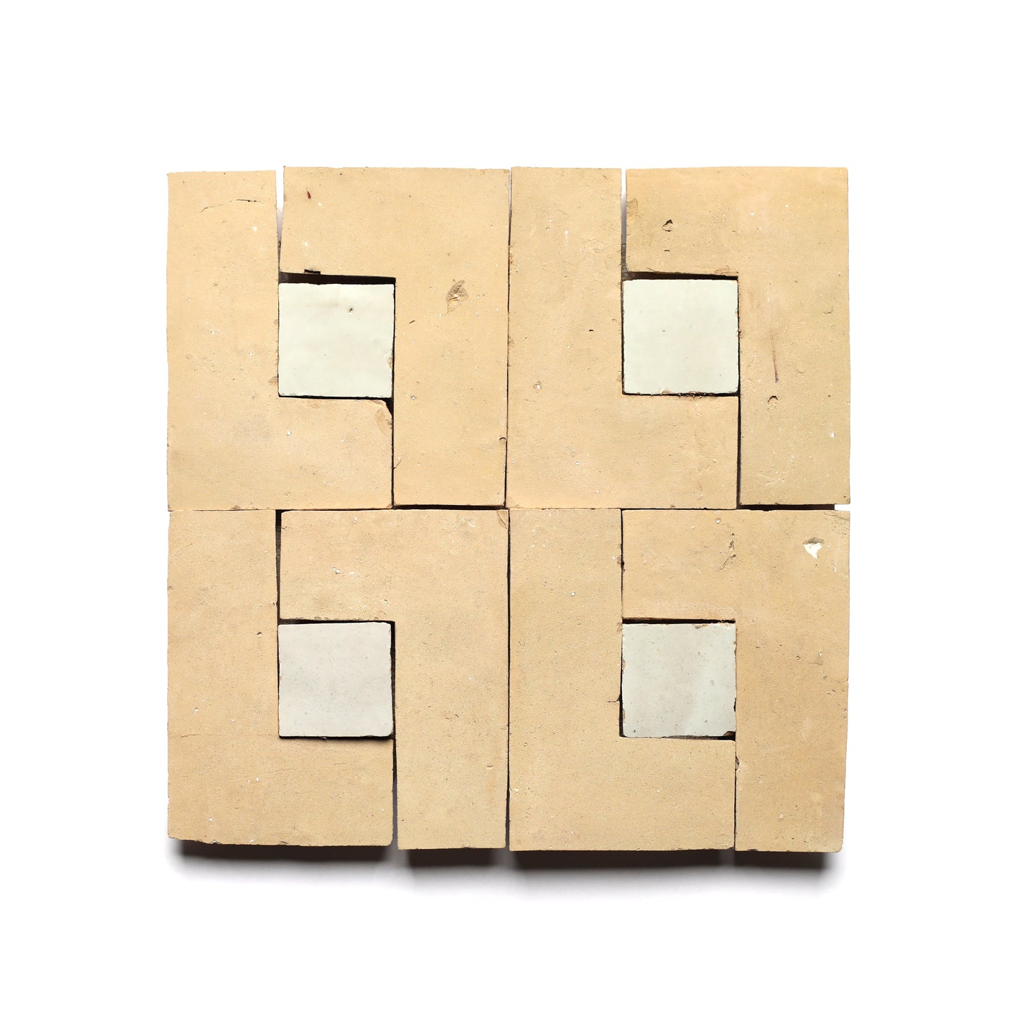 Four Rubric 2 tiles by Zia Tile, in tan with intricate cut-out patterns and light central squares, create a geometric, symmetrical look—ideal for a chic kitchen backsplash.