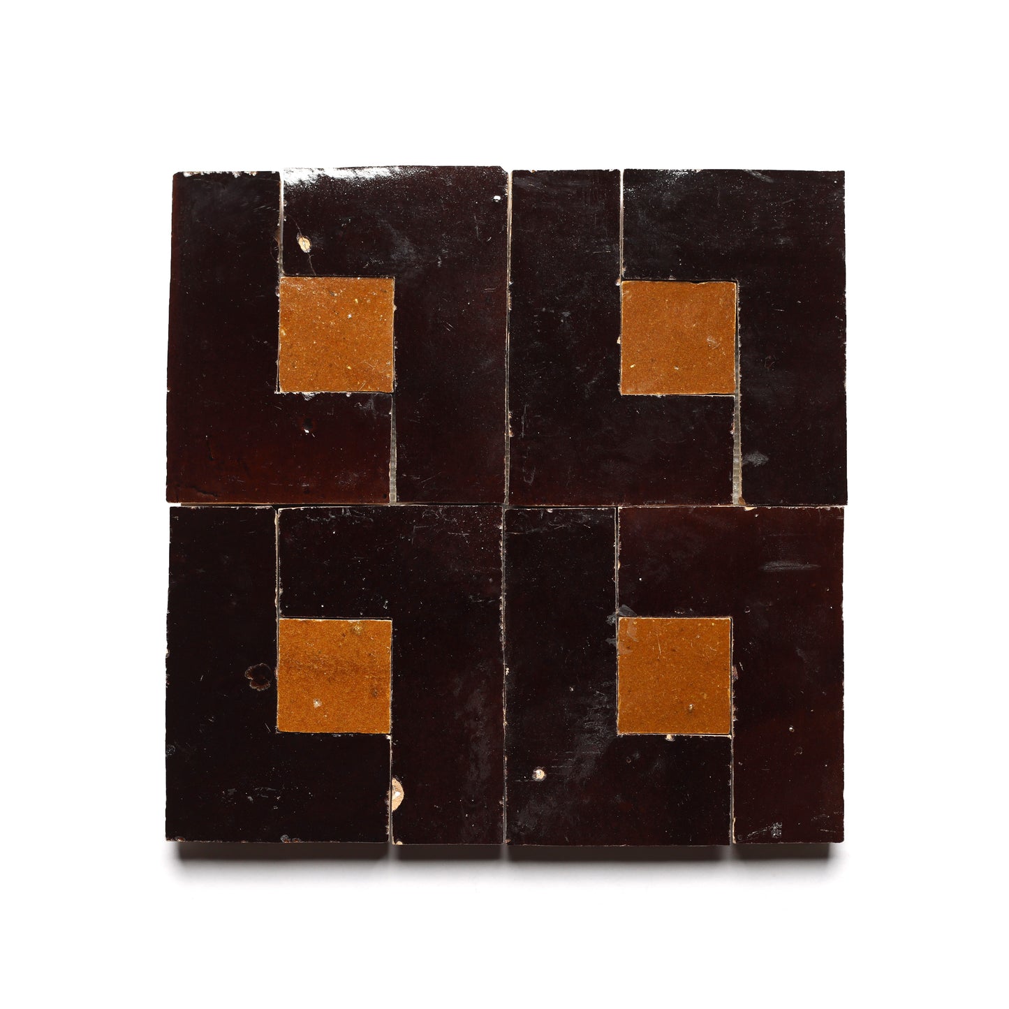 The Rubric 5 tile by Zia Tile features a geometric pattern with dark brown and mustard segments, forming a symmetrical design centered on a mustard square against white, echoing classic Moroccan craftsmanship.