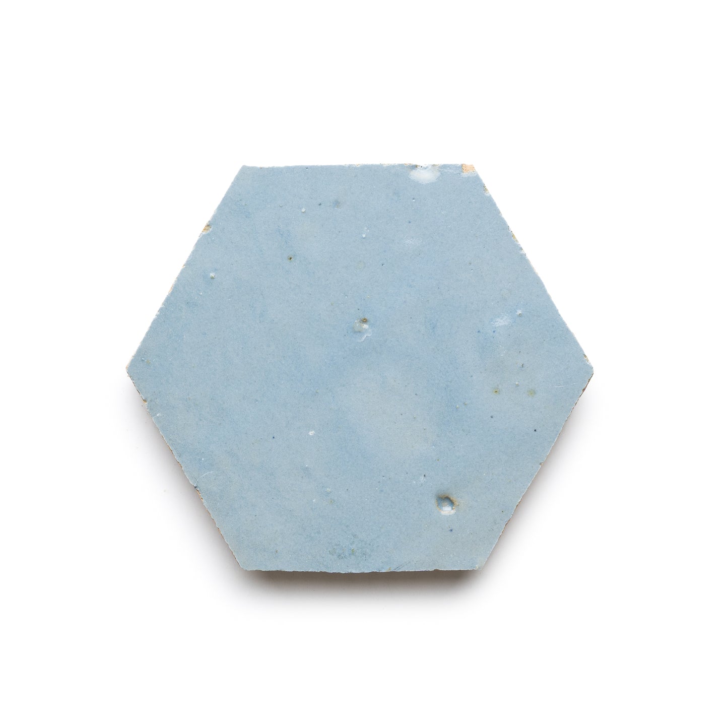 The Skylight Hex is a single flat hexagonal ceramic tile in smooth light blue with minor imperfections, shown on a white background—perfect as a kitchen backsplash or for adding Moroccan charm. Part of the Skylight Hex Zellige Tiles collection.