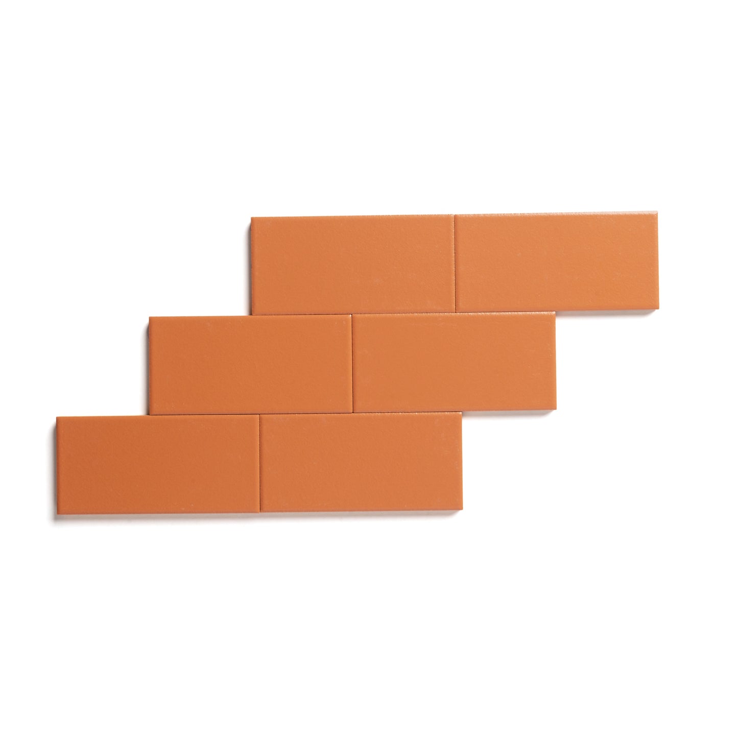 Six Tangelo 2x4 orange matte ceramic tiles by Zia Tile are arranged in a staggered, brick-like pattern on a white background, highlighting the versatility of these architectural grade tiles.