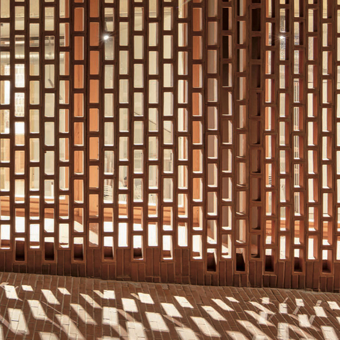 Block + Red Earth by Zia Tile features vertically arranged rectangular red bricks with gaps that let sunlight create patterned shadows on terra cotta tiles covering the floor.