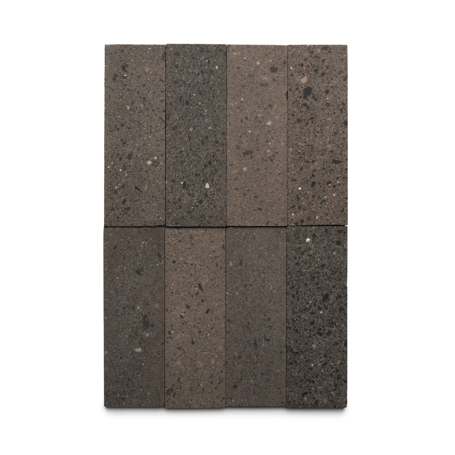 Eight rectangular Volcan 4x12 tiles by Zia Tile are arranged in two columns and four rows on a white background. The dark gray, volcanic Cantera stone tiles feature a slightly rough, speckled surface.