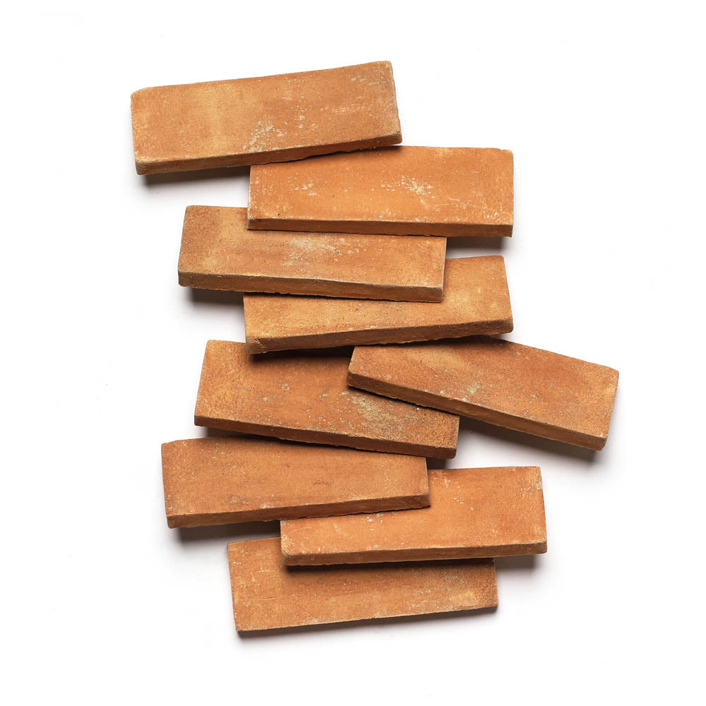 Ten 2x6 Rectangle + Fired Earth tiles from Zia Tile are arranged in a staggered, overlapping pattern on a white background, highlighting their handcrafted terracotta look.