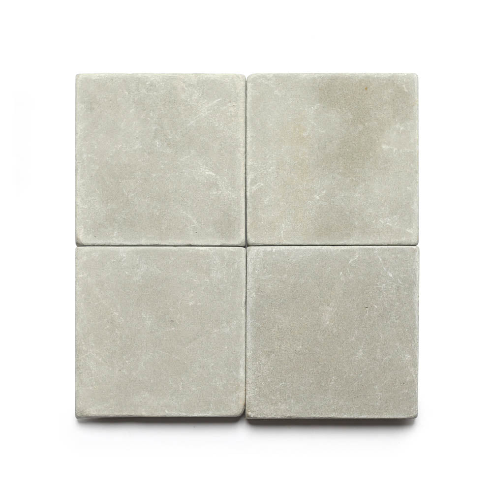 Four Monument 6x6 + Honed limestone tiles in light grey, arranged in a 2x2 grid on a white background, highlighting their subtle texture and gentle color variations.