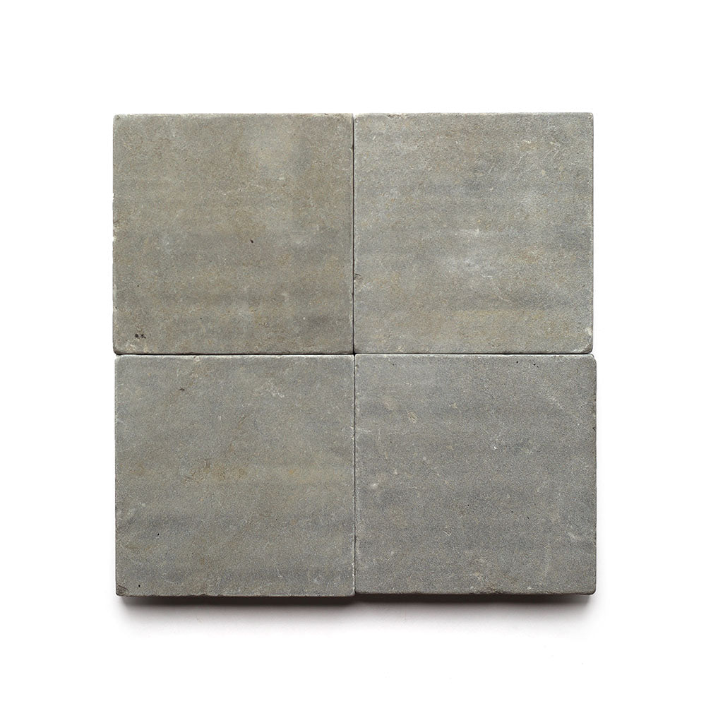 Four square, gray Basilica 6x6 + Honed tiles from Zia Tile are arranged in a 2x2 grid on a white background, showcasing a smooth matte finish and subtle natural variations for an understated yet elegant look.