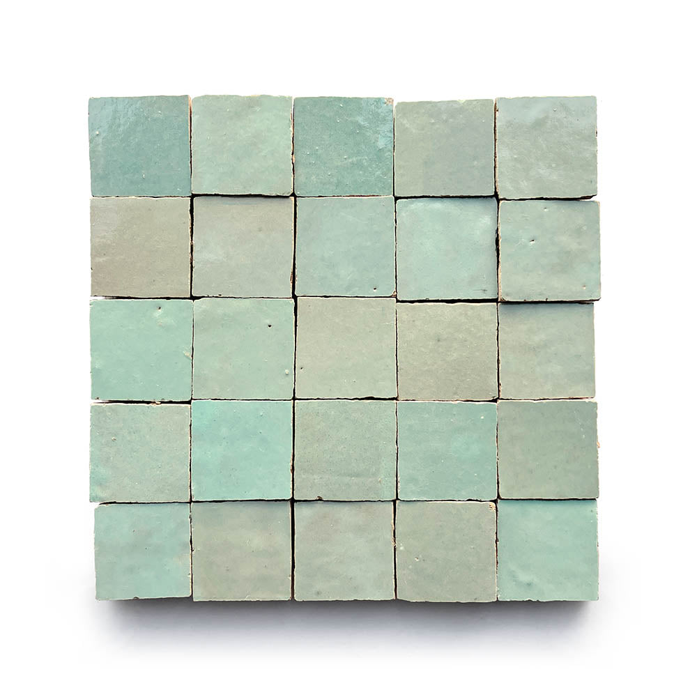 A square grid of 25 Absinthe 2x2 tiles in textured light blue and green hues, set against a white background, highlights the classic Moroccan tile craftsmanship.