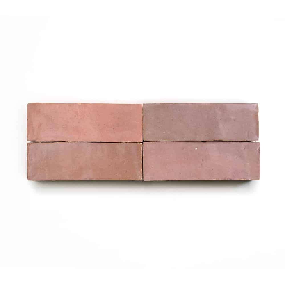 Four Desert Bloom 2x6 tiles from Zia Tile, in a reddish-pink hue, are arranged in two rows on a white background, forming a simple rectangular block inspired by classic Moroccan design.