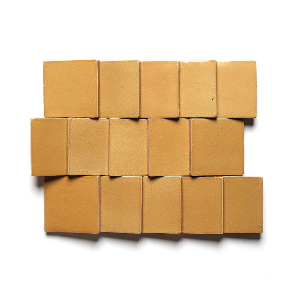 Fourteen square, light brown Dorado 4x4 tiles by Zia Tile are laid in three uneven rows on a white background, creating a staggered pattern inspired by classic San Miguel de Allende designs.