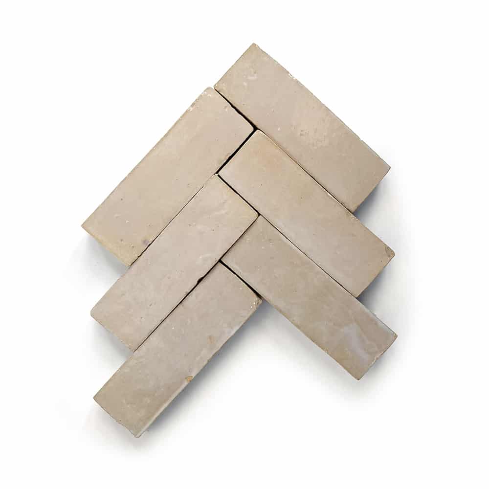 Five Glazed Earth 2x6 tiles by Zia Tile, in beige and rectangular, are laid in a herringbone pattern on a white background—ideal inspiration for a chic kitchen backsplash.