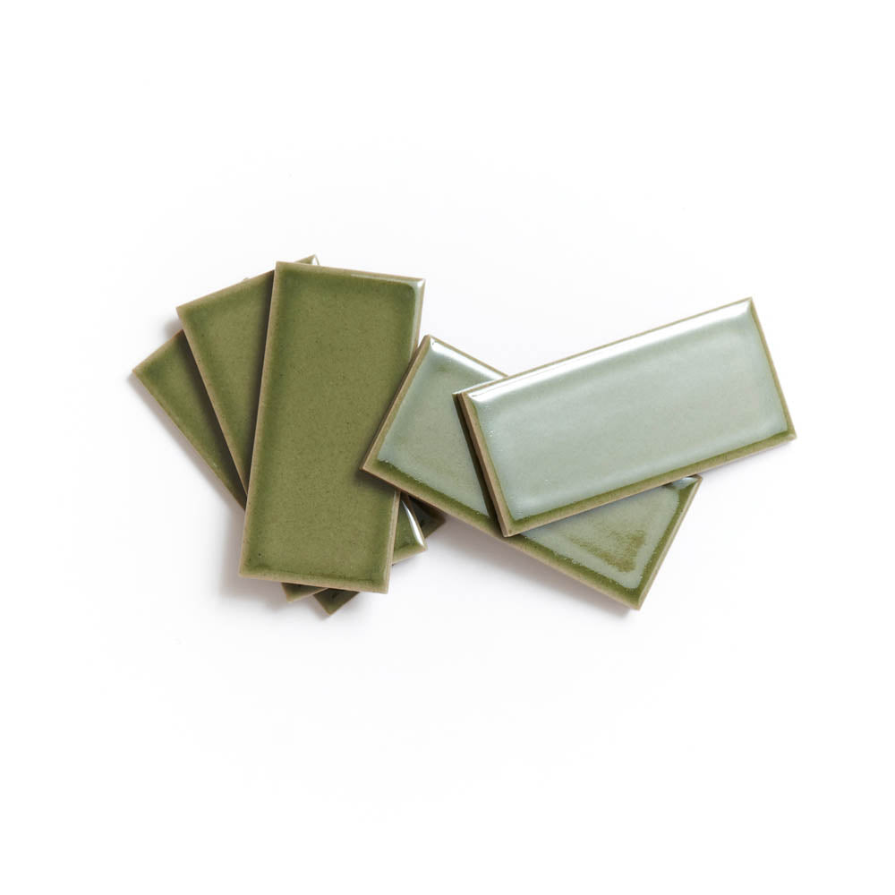 Six Kelp Forest 2x4 ceramic tiles by Zia Tile, in varying green shades, are arranged in a slightly overlapping, fanned-out pattern atop a white background.