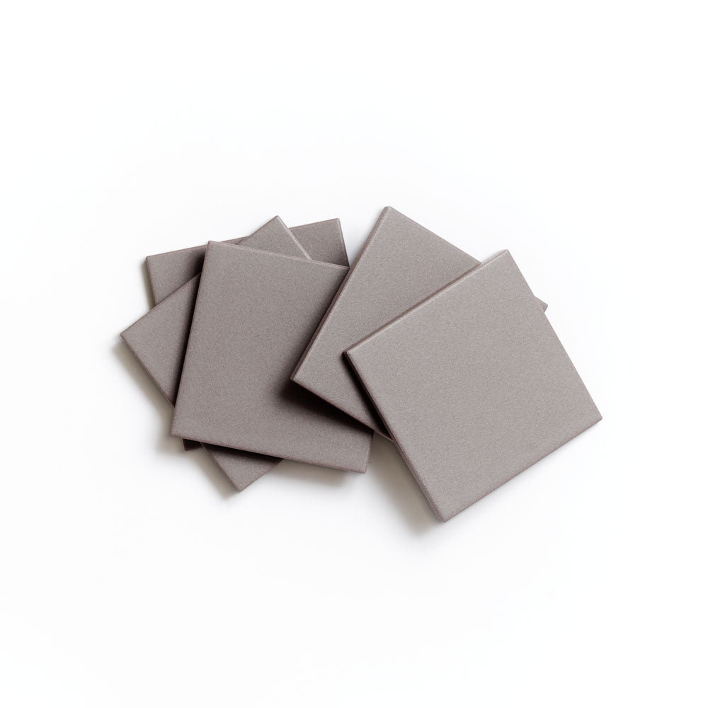 Six Portland Grey 4x4 foam pads by Zia Tile are stacked in a slightly overlapping pattern, resembling matte ceramic tile, on a white background.