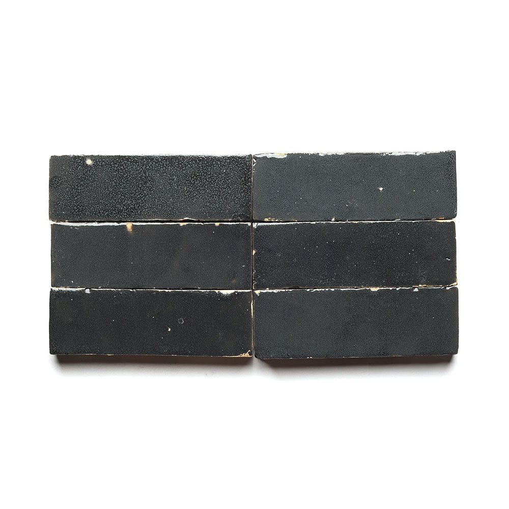 Six rectangular black soap bars are arranged in two rows of three on a white background, their rough surfaces and visible edges echoing the look of Zia Tiles Slate Grey 2x6 tiles.