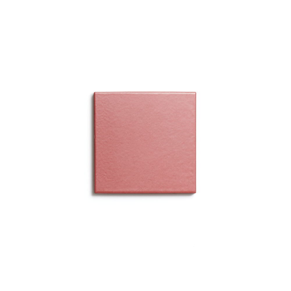A single Wild Fig 4x4 ceramic tile by Zia Tile, featuring a smooth matte pink finish, is centered on a plain white background, showcasing the refined look of architectural grade tiles.