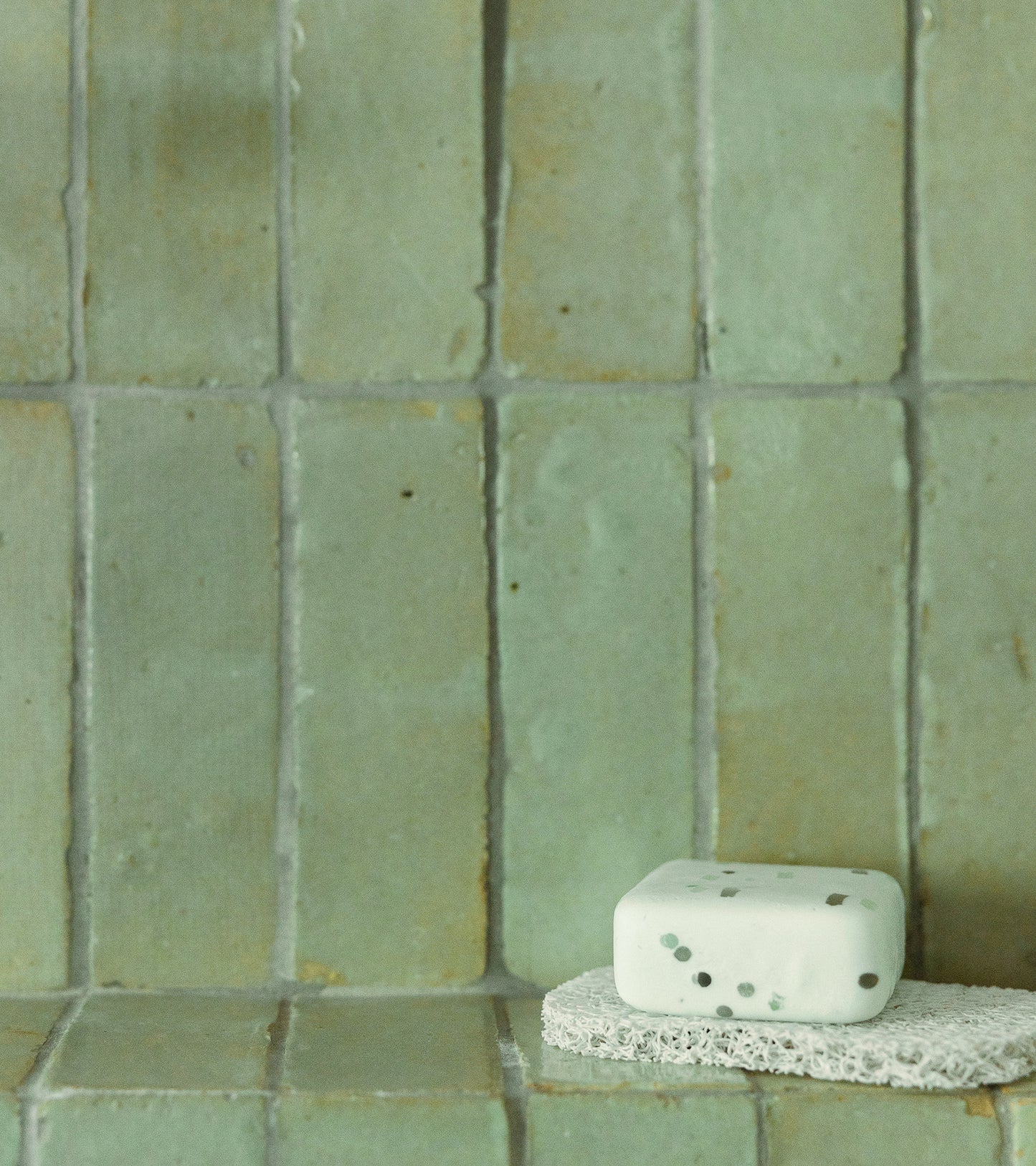 A sponge rests on the counter, just beneath a stunning Zia Tile Absinthe 2x6 Moroccan tile backsplash, adding a touch of artistry to the space.