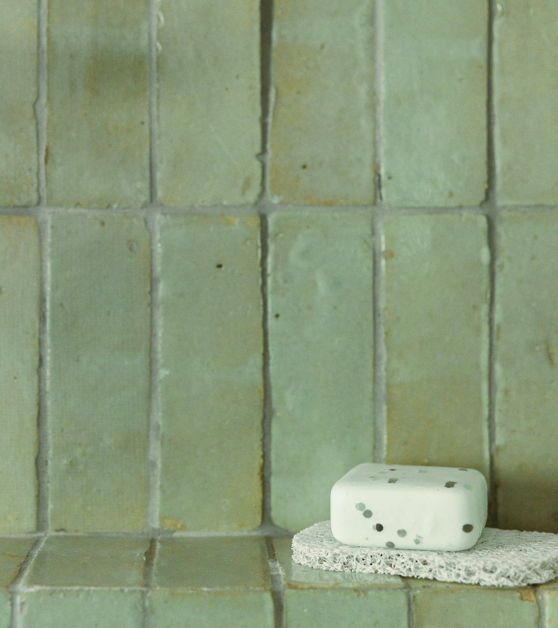 A sponge rests on the counter, just beneath a stunning Zia Tile Absinthe 2x6 Moroccan tile backsplash, adding a touch of artistry to the space.
