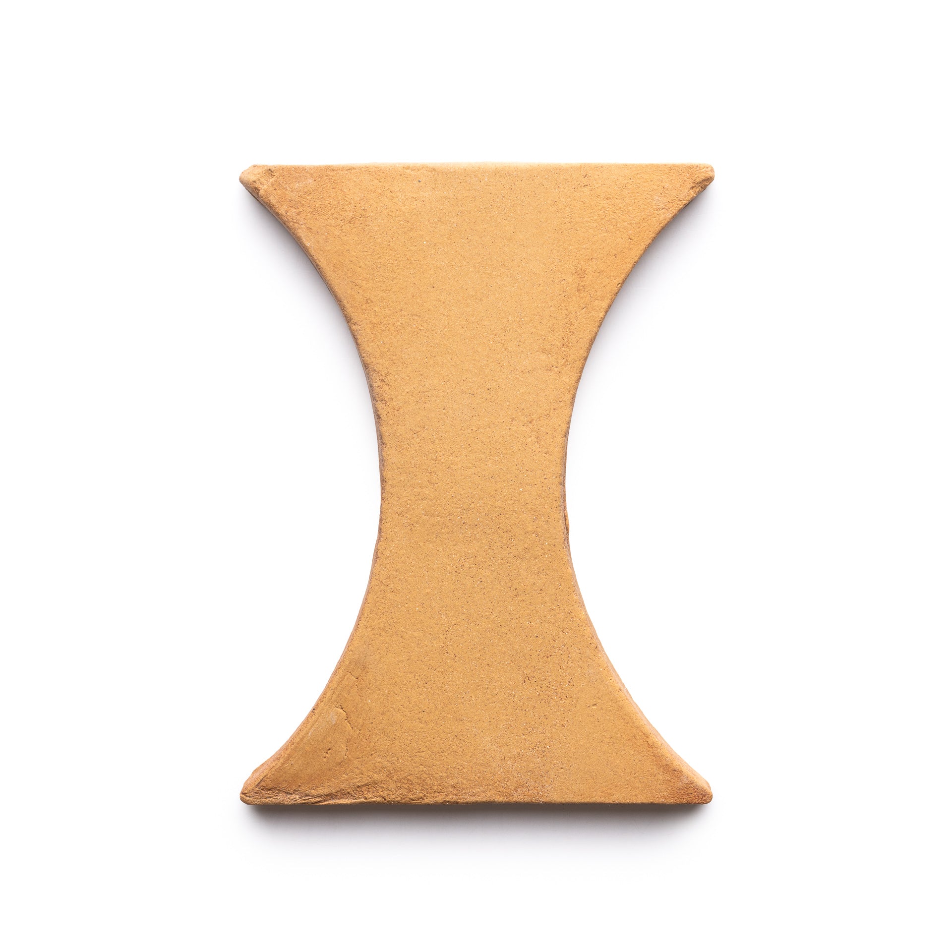 The Oaxaca + Adobe tile by Zia Tile is a tan, hourglass-shaped ceramic tile with smooth surfaces and subtly rounded edges, shown on a white background.