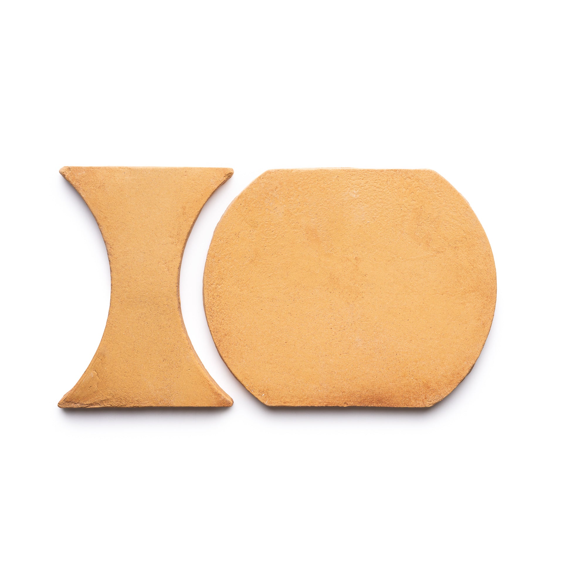 The Oaxaca + Adobe tiles by Zia Tile, one hourglass-shaped and one rounded rectangle in tan, are displayed side by side on a white background.