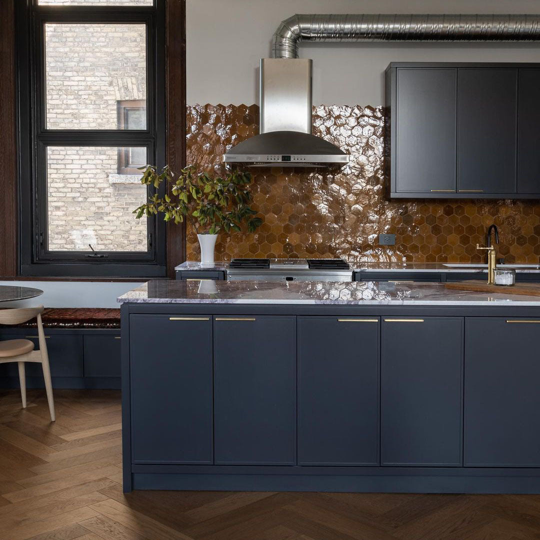 Shimmering Amber hexagon zellige tiles on a kitchen backsplash, with wood floors and grey blue cabinets.