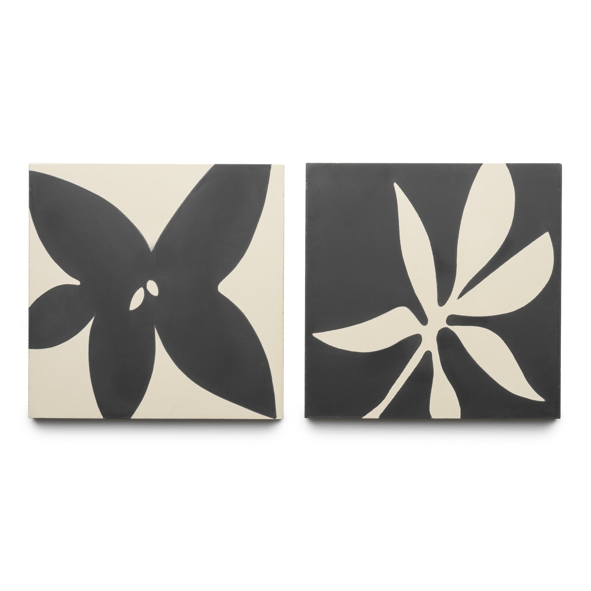 The Flora 8x8 Set Black + Bone by Zia Tile features two square tiles: one with a bold four-petal flower and the other with an abstract, multi-tipped leaf, both in striking black and white designs.