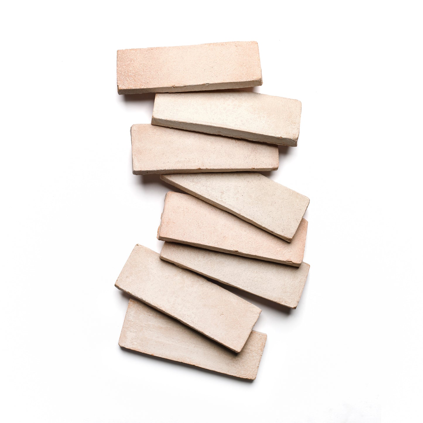 Seven 2x6 Rectangle + Blanco tiles by Zia Tile, in a soft beige reminiscent of handmade Cotto, are arranged in a subtle zigzag on a white background.