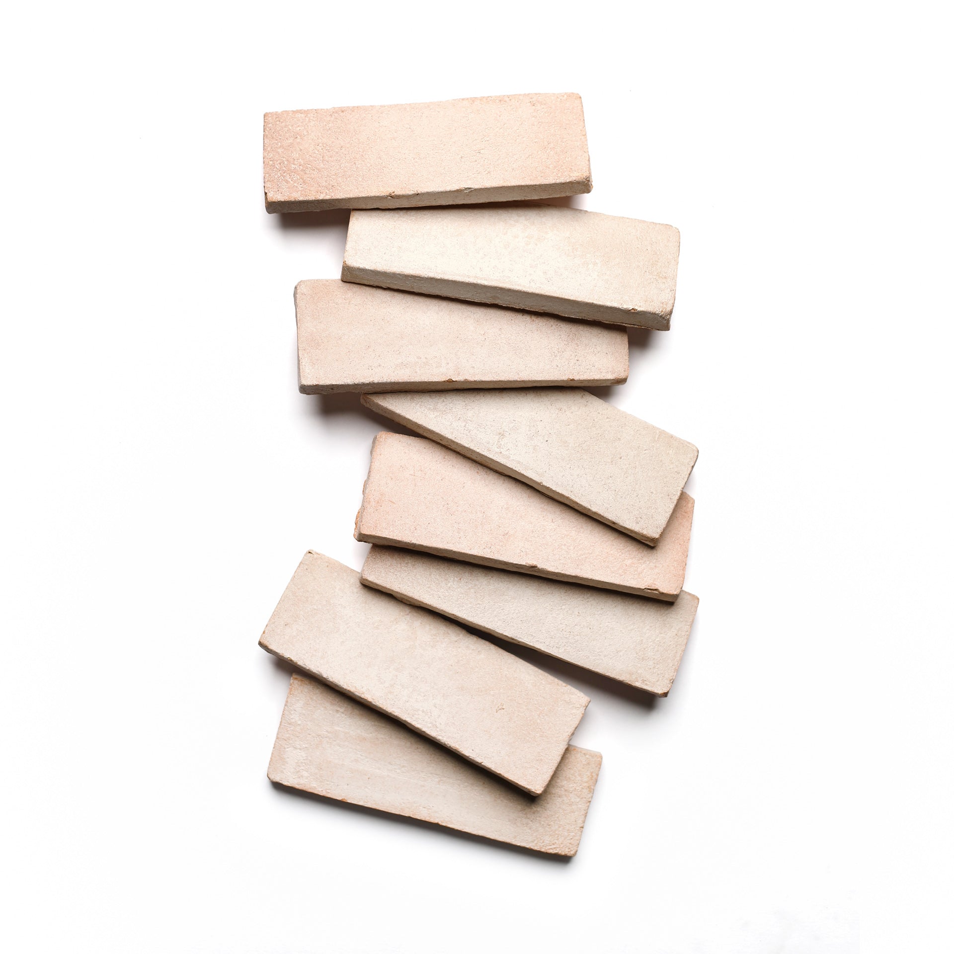 Seven 2x6 Rectangle + Blanco tiles by Zia Tile, in a soft beige reminiscent of handmade Cotto, are arranged in a subtle zigzag on a white background.