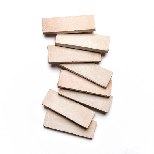 Seven 2x6 Rectangle + Blanco tiles by Zia Tile, in a soft beige reminiscent of handmade Cotto, are arranged in a subtle zigzag on a white background.