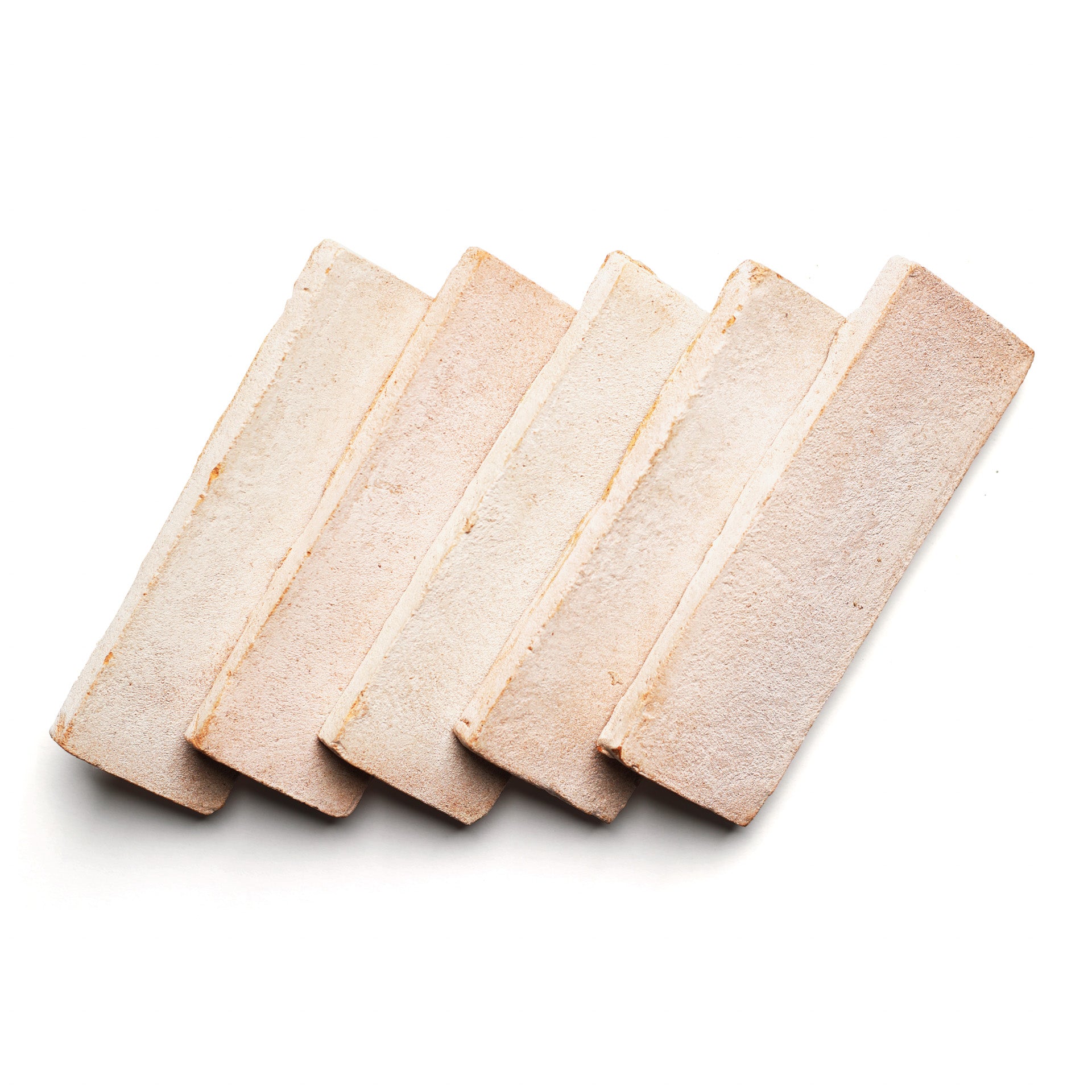 Five 2x6 Rectangle + Blanco tiles by Zia Tile, arranged in a slightly fanned-out row on a white background, showcase handmade character and warm hues inspired by ceramic arts.