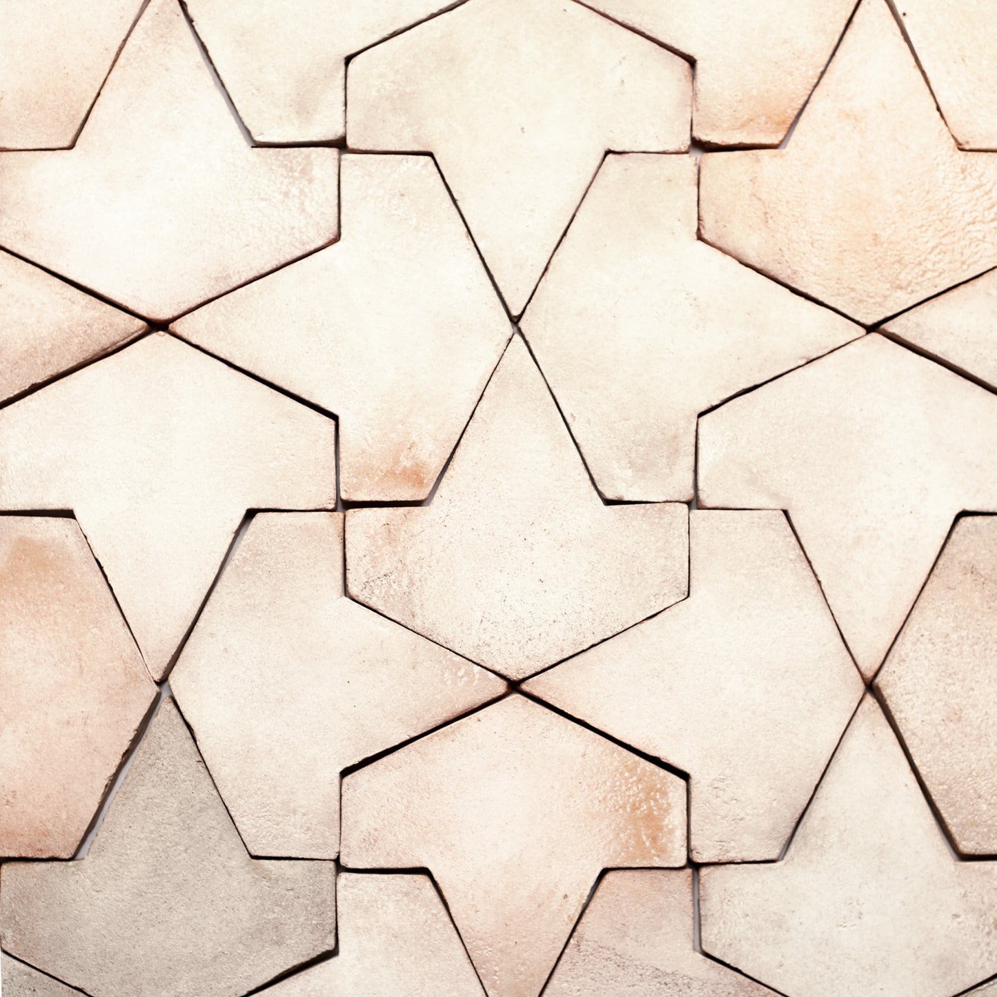 Close-up of Alcazar + Blanco tiles by Zia Tile, featuring beige and light brown handmade-style Cotto in a repeating star-like geometric pattern with subtle color and texture variations.