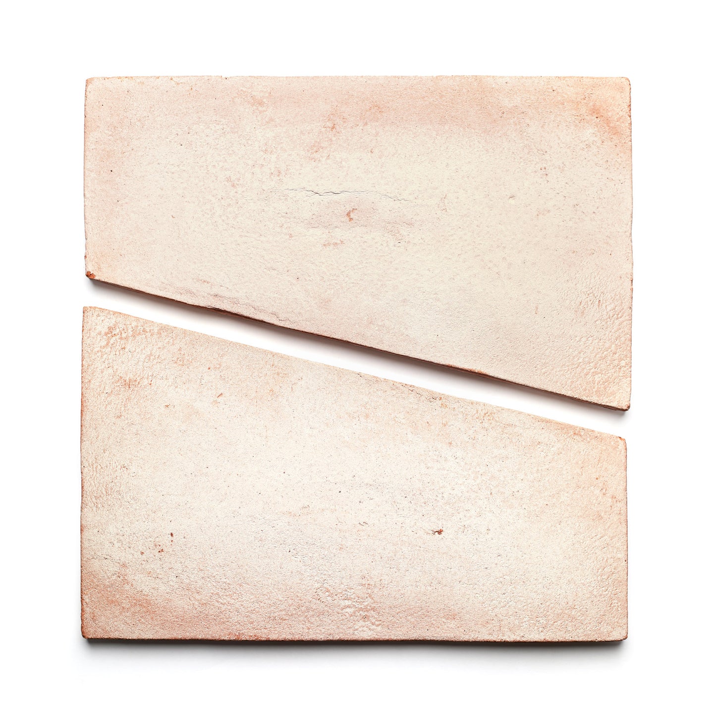 Two Toltec + Blanco tiles by Zia Tile, featuring a light pink hue and handmade texture, are placed on a white background—one whole and one diagonally cut—to create a striking geometric composition.