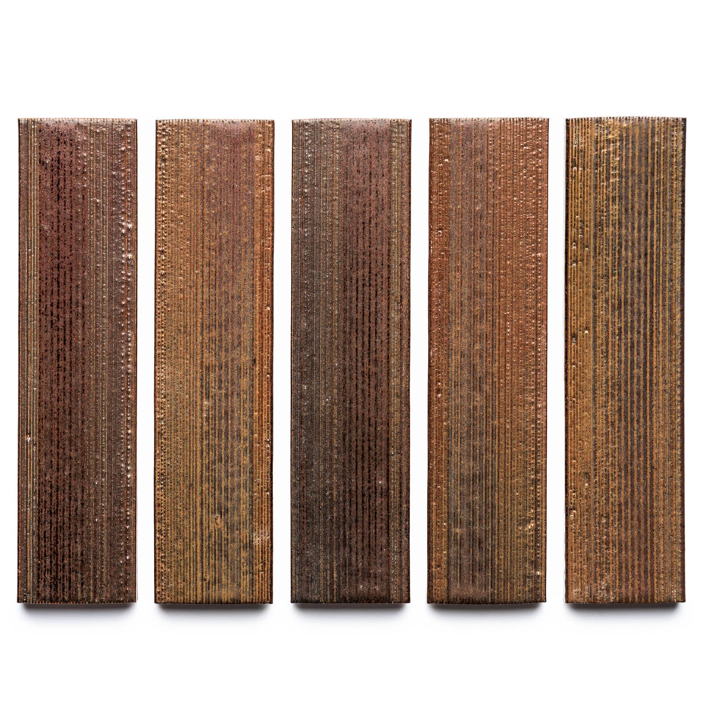 Buckeye + Etched by Zia Tile features five rectangular panels in brown and copper, each with vertical grooves and a metallic sheen, displayed side by side against a white background.