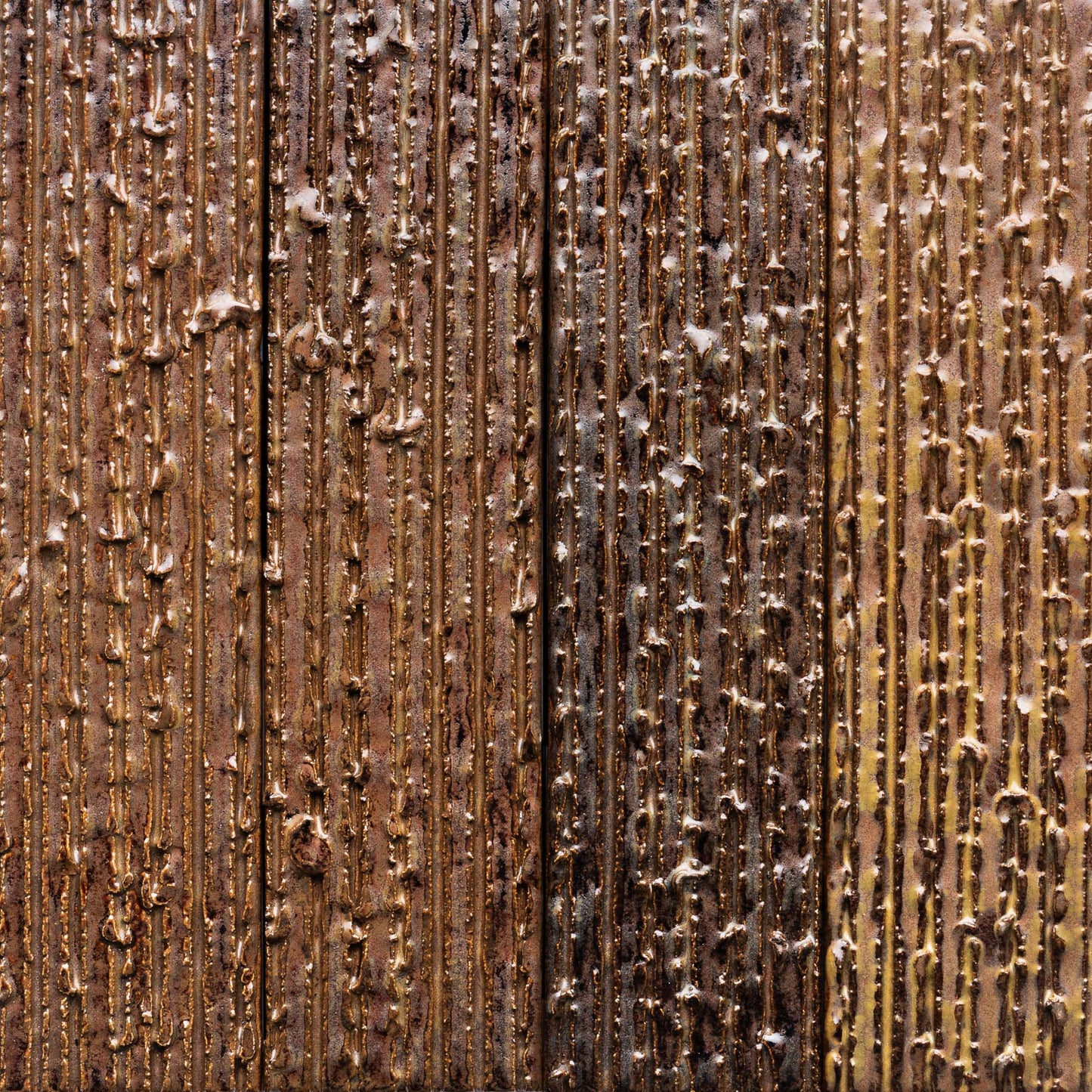 Close-up of Zia Tile's Buckeye + Furrowed tile, featuring a textured vertical wood-like surface with lines and raised spots in a glossy, uneven brown and gold finish for a rustic, weathered look.