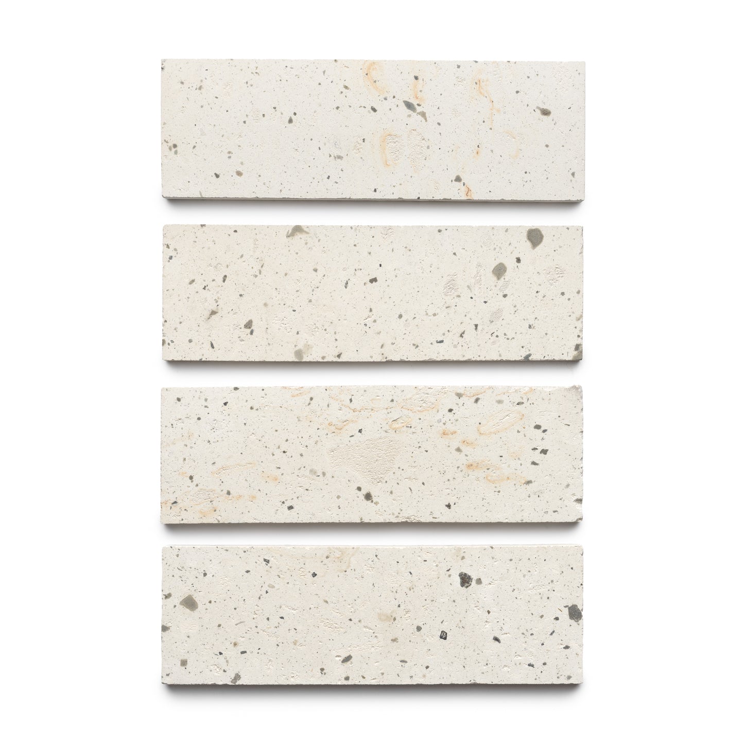 Four Caldera 4x12 rectangular terrazzo tiles by Zia Tile, off-white with scattered dark and light specks, are arranged vertically on a plain white background.