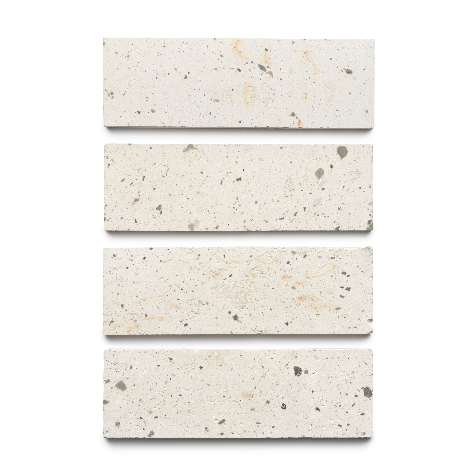 Four Caldera 4x12 rectangular terrazzo tiles by Zia Tile, off-white with scattered dark and light specks, are arranged vertically on a plain white background.