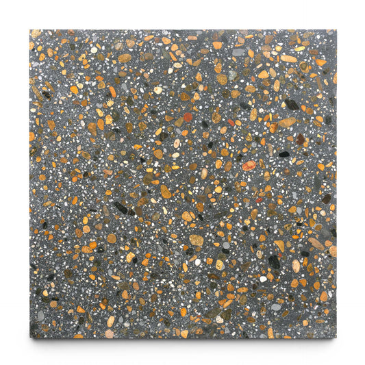 The Calypso 24x24 by Zia Tile is a handmade square tile with a dark gray base, highlighted by scattered fragments of yellow, orange, brown, and black stones for a richly speckled and textured look.