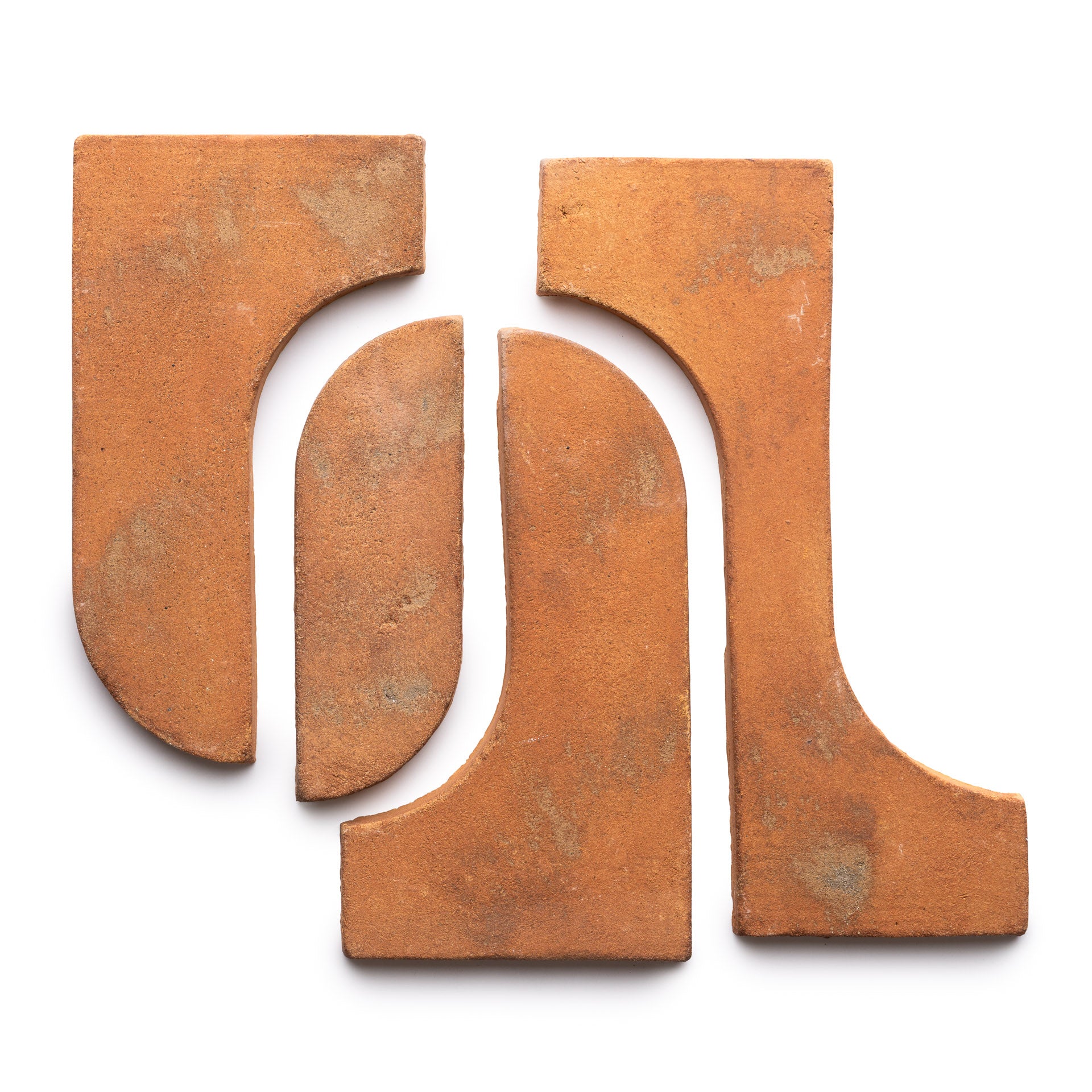 Four Durango + Fired Earth terracotta tiles by Zia Tile are arranged on a white background, creating an abstract, symmetrical pattern with geometric cutouts and curving angles.