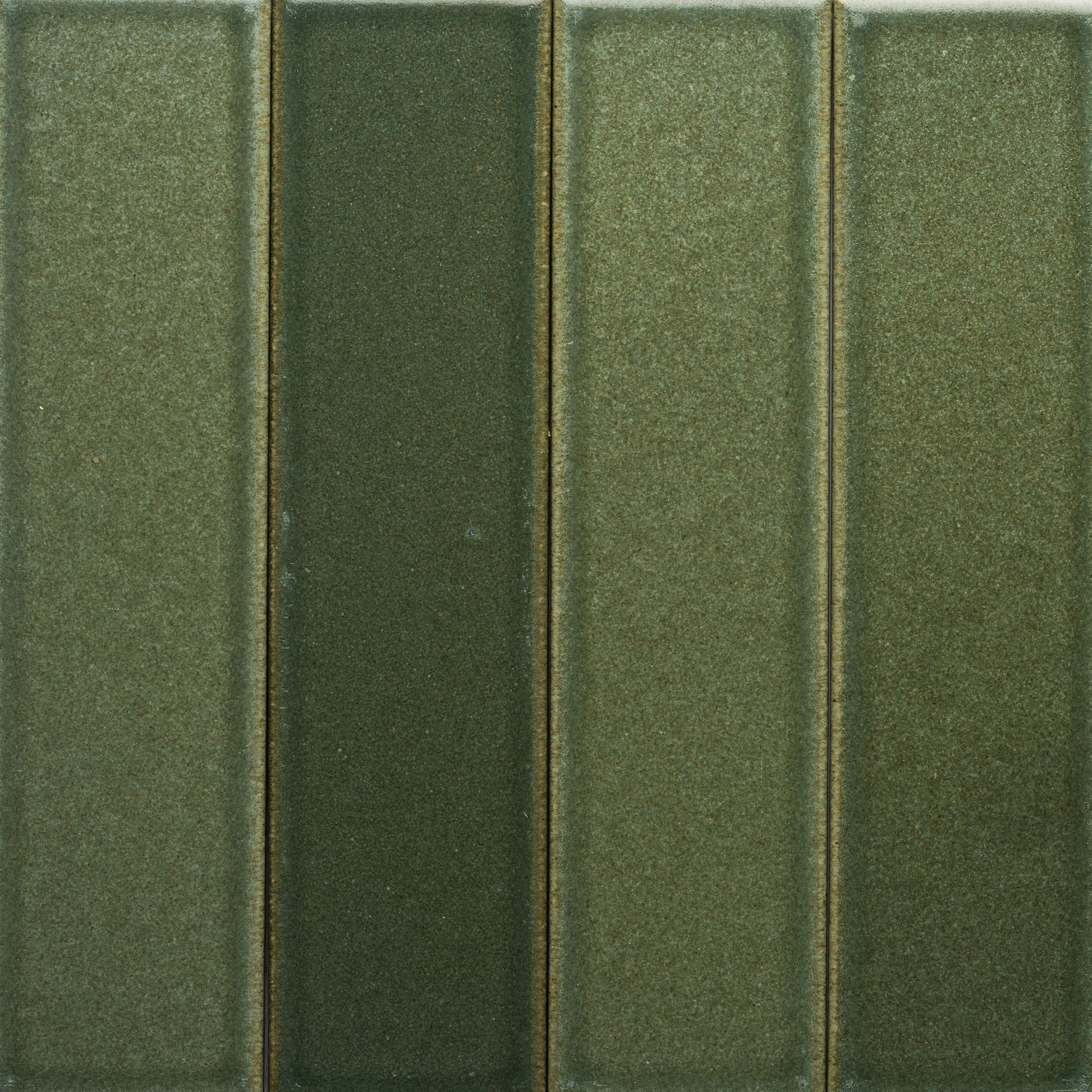 A close-up of four vertical, rectangular Frogtown + Flat green tiles by Zia Tile, each in slightly different shades, arranged side by side with a smooth, matte finish and subtle texture.