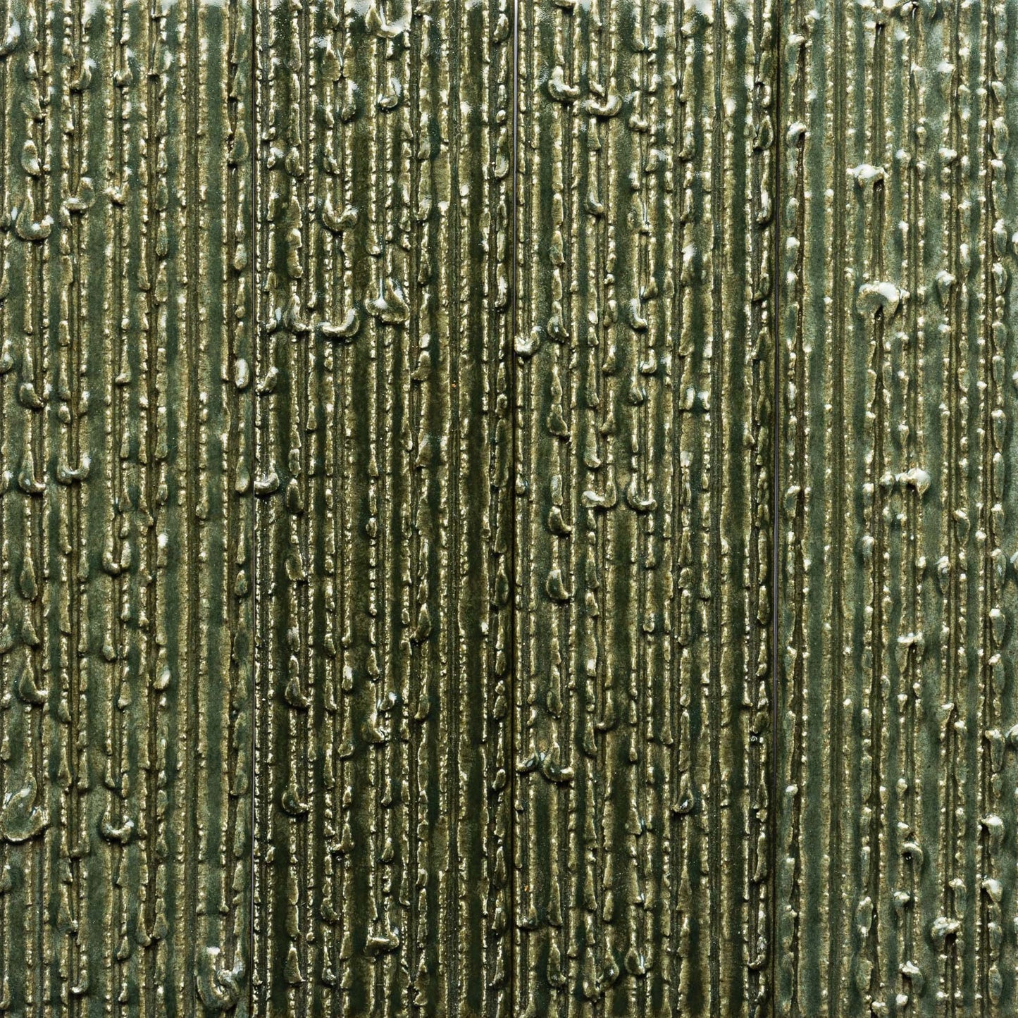 Close-up of Zia Tile’s Frogtown + Furrowed: a textured metallic green tile with vertical, irregular raised lines and small bumps, forming an abstract, industrial pattern with shiny, reflective areas.
