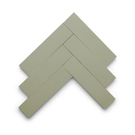 Five rectangular Gypsum 2x8 tiles by Zia Tile in sage green are arranged in a herringbone pattern on a white background.