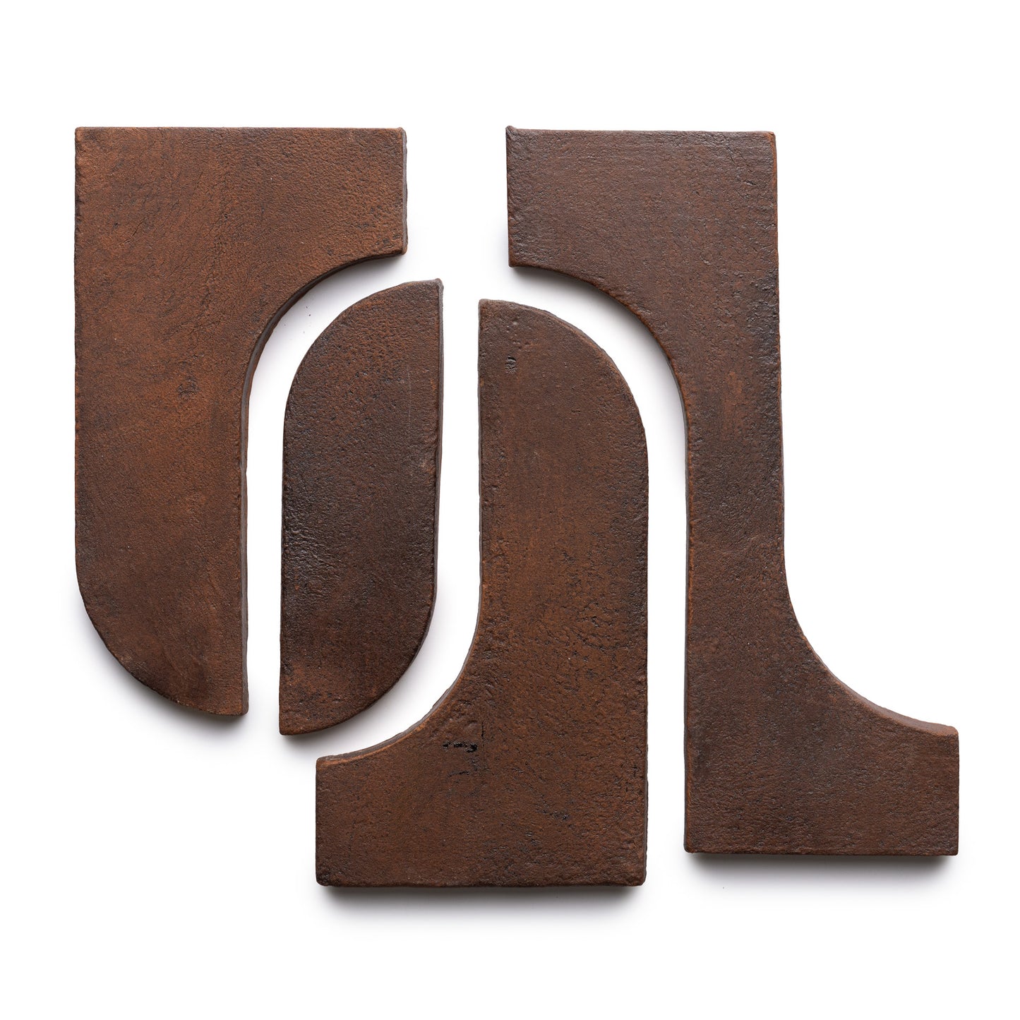 Four rust-colored, textured metal pieces from Zia Tile’s Durango + Madera collection are arranged on a white background, forming an abstract geometric composition with both curved and straight edges.