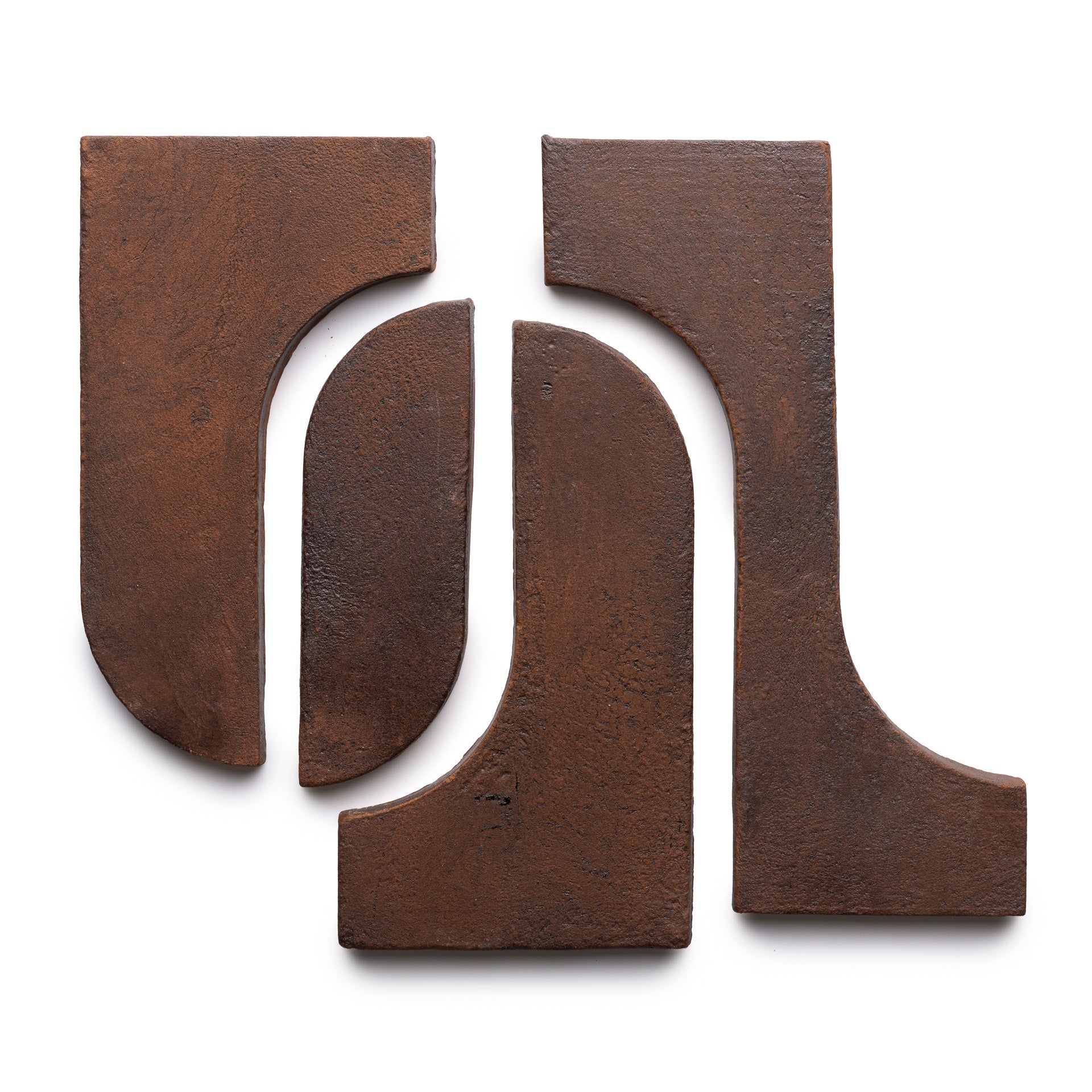 Four rust-colored, textured metal pieces from Zia Tile’s Durango + Madera collection are arranged on a white background, forming an abstract geometric composition with both curved and straight edges.