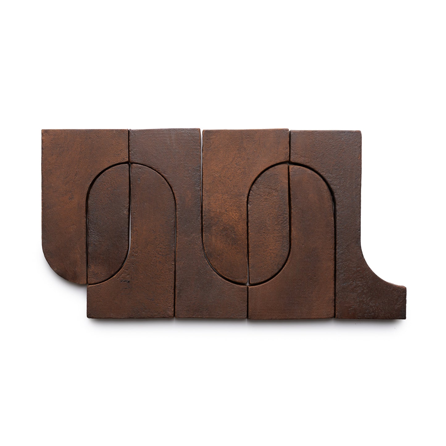 Six interlocking Durango + Madera rectangular bronze tiles by Zia Tile feature curved cutouts forming an abstract pattern on a white background. Their dark brown metal surfaces have a subtly mottled texture.
