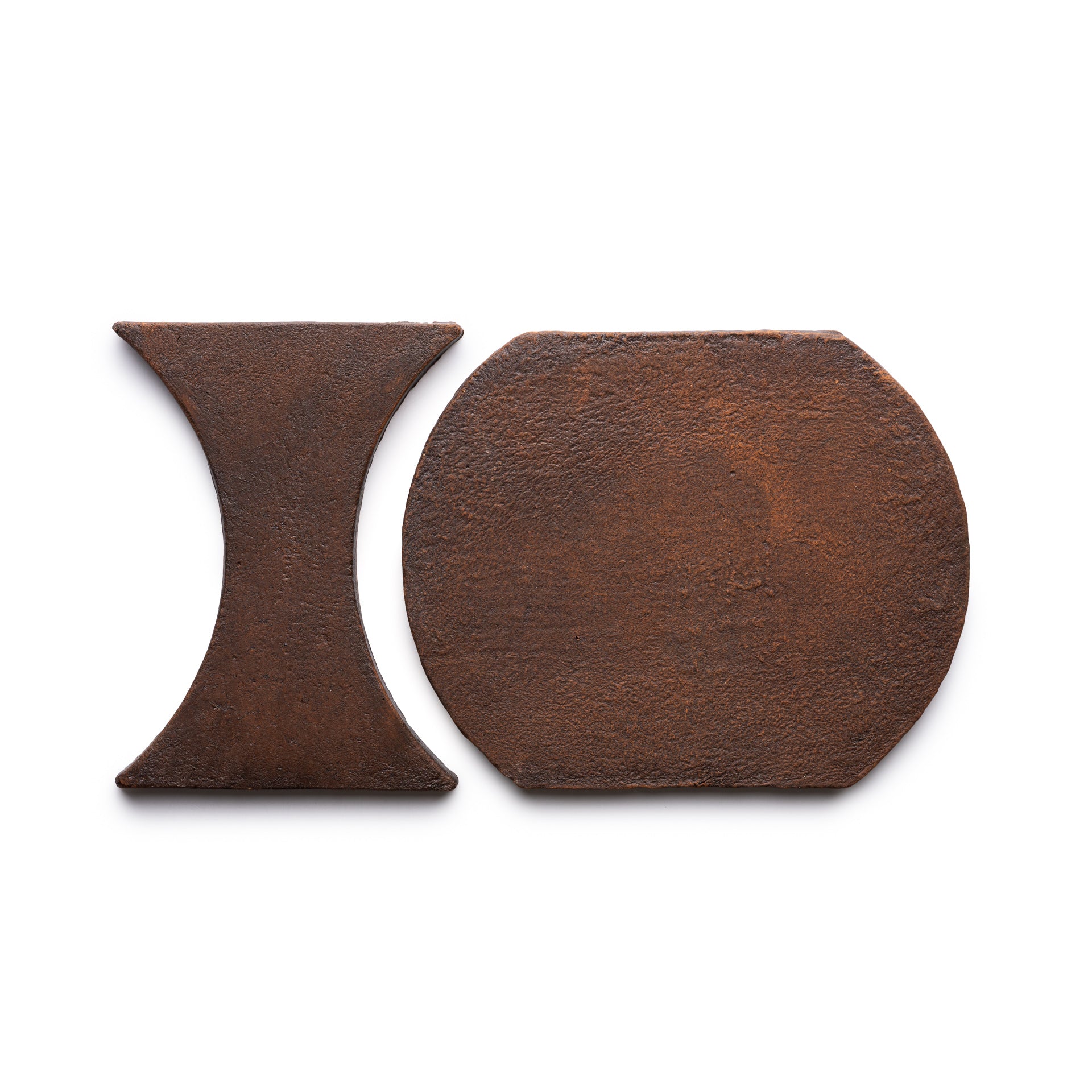 Two rusty metal pieces, Oaxaca + Madera by Zia Tile, are shown on a white background: one is hourglass-shaped and the other has a rounded rectangle shape.