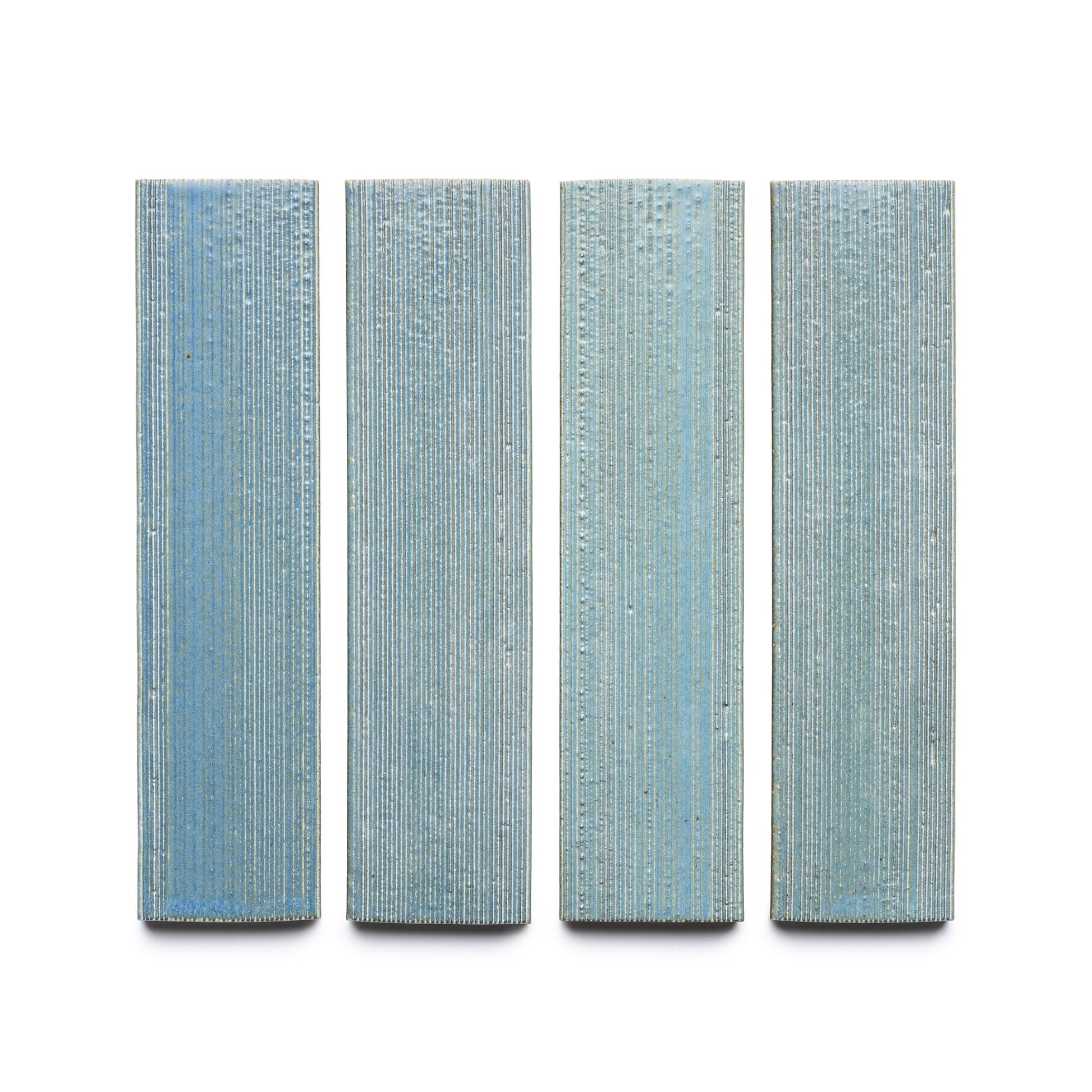 Four vertically oriented, rectangular Morning Light + Etched tiles by Zia Tile, in blue with a textured linear pattern, evenly spaced against a white background.
