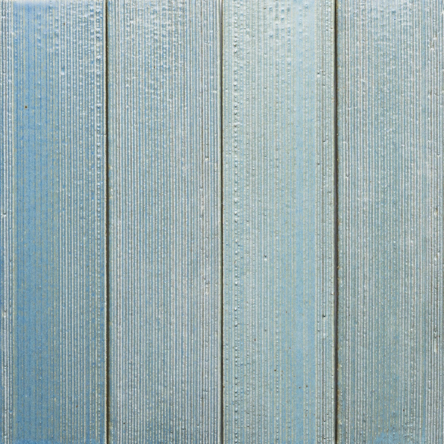 Close-up of four vertical "Morning Light + Etched" panels by Zia Tile, painted light blue with a textured, ribbed surface and subtle color and grain variations.