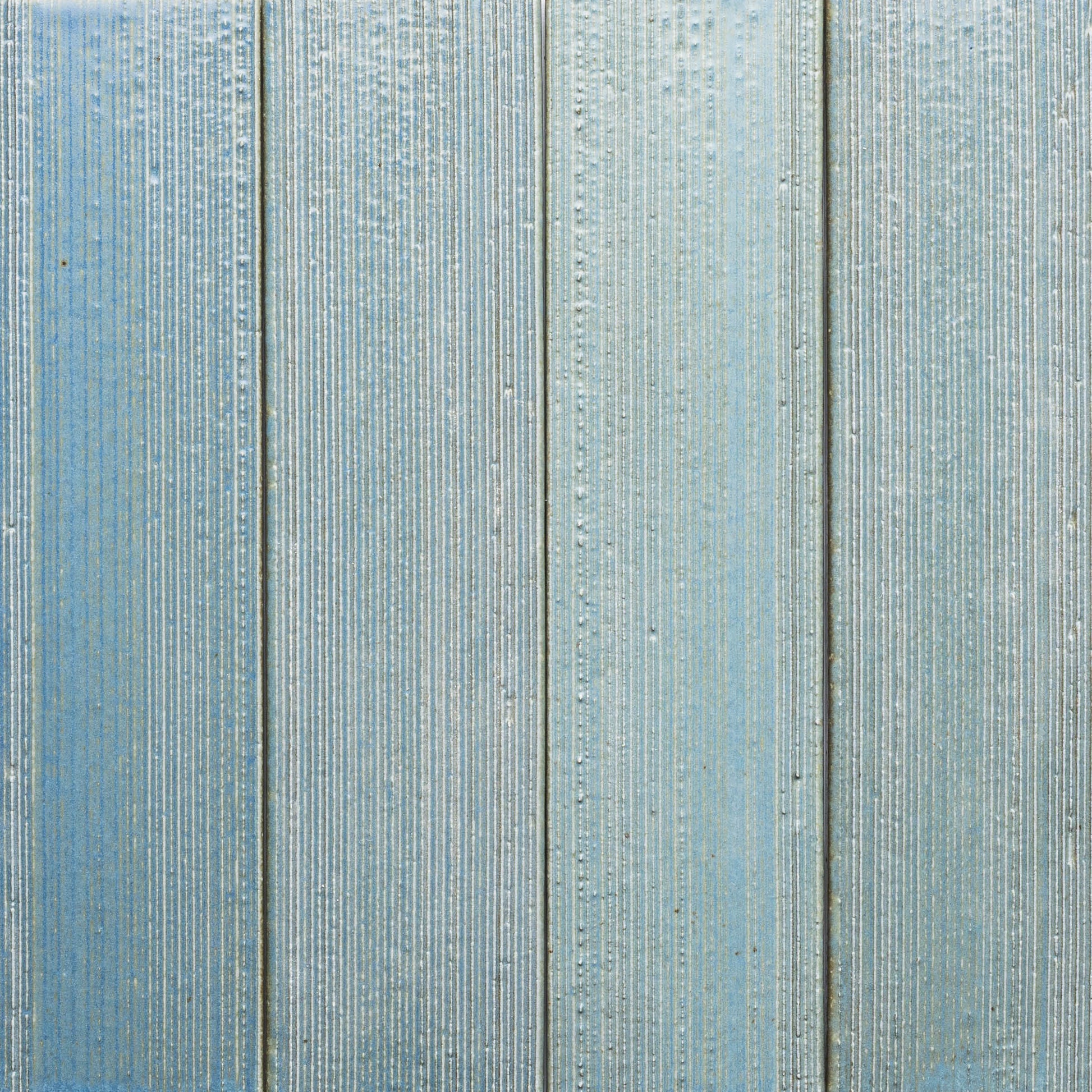 Close-up of four vertical "Morning Light + Etched" panels by Zia Tile, painted light blue with a textured, ribbed surface and subtle color and grain variations.